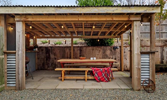 large wooden table with bench seating, charcoal BBQ with tools, lighting and power socket